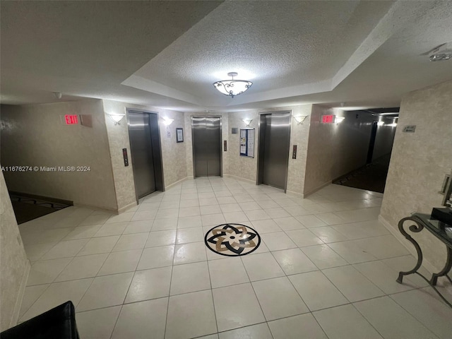 hall featuring a raised ceiling, elevator, and a textured ceiling