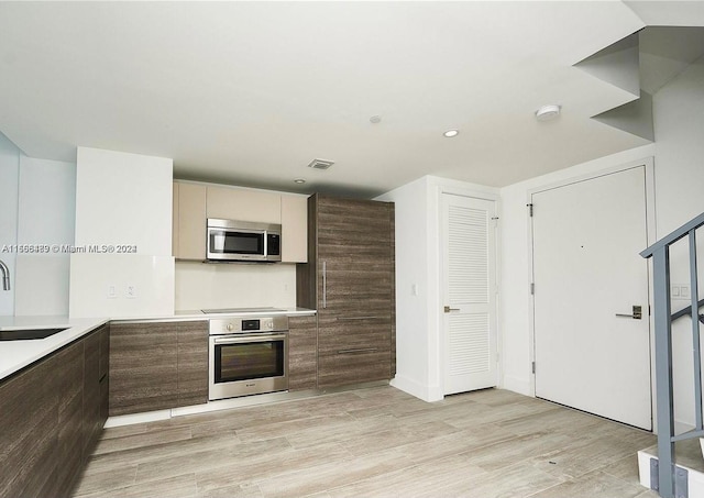 kitchen with appliances with stainless steel finishes, sink, and light hardwood / wood-style floors