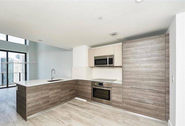 kitchen with appliances with stainless steel finishes, kitchen peninsula, sink, and light wood-type flooring