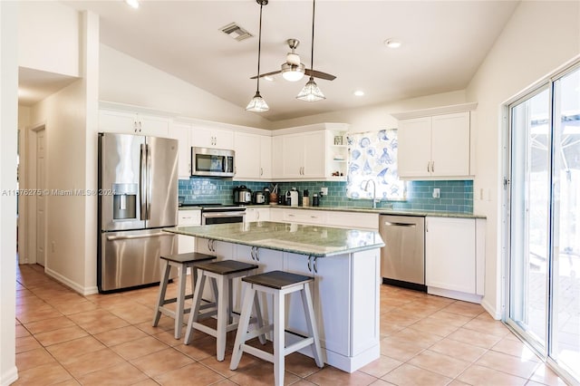 kitchen with white cabinets, appliances with stainless steel finishes, a kitchen island, and vaulted ceiling