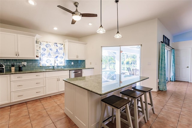 kitchen with a kitchen island, light stone counters, white cabinets, sink, and light tile patterned floors