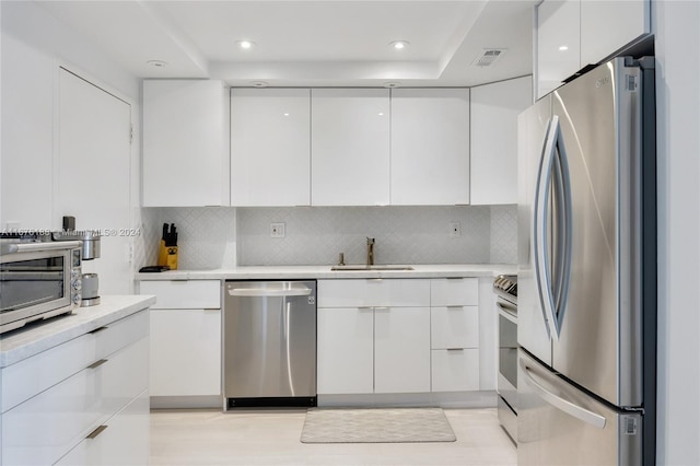 kitchen featuring backsplash, white cabinets, appliances with stainless steel finishes, and sink