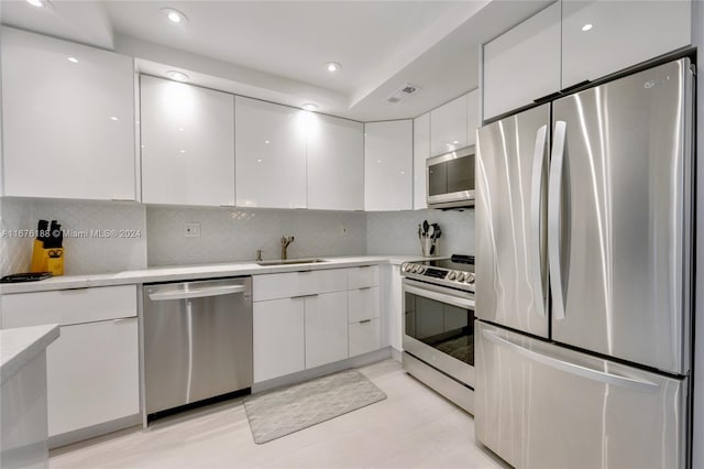 kitchen with sink, light hardwood / wood-style flooring, white cabinetry, appliances with stainless steel finishes, and decorative backsplash