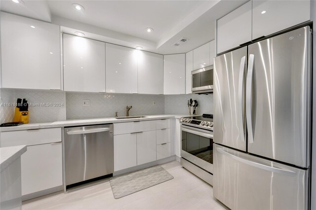 kitchen featuring recessed lighting, modern cabinets, a sink, white cabinets, and appliances with stainless steel finishes