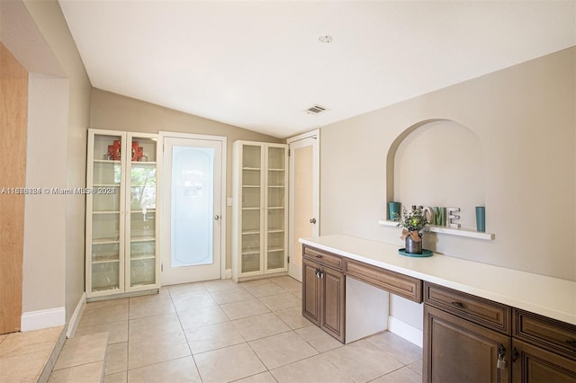 doorway to outside with vaulted ceiling, light tile patterned floors, and built in desk