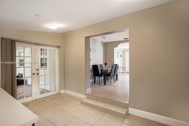 doorway with arched walkways, light tile patterned floors, french doors, and baseboards