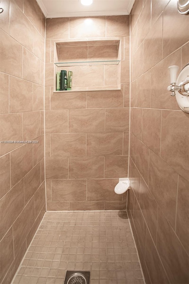 full bathroom featuring a tile shower and crown molding