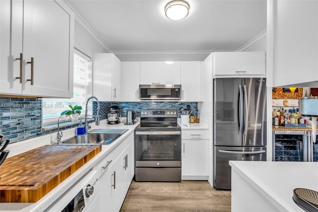 kitchen featuring stainless steel appliances, sink, white cabinetry, light hardwood / wood-style flooring, and ornamental molding