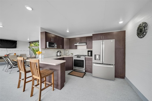 kitchen with sink, kitchen peninsula, dark brown cabinets, stainless steel appliances, and a kitchen breakfast bar