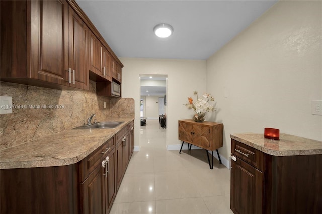 kitchen featuring dark brown cabinetry, sink, light tile patterned floors, and backsplash