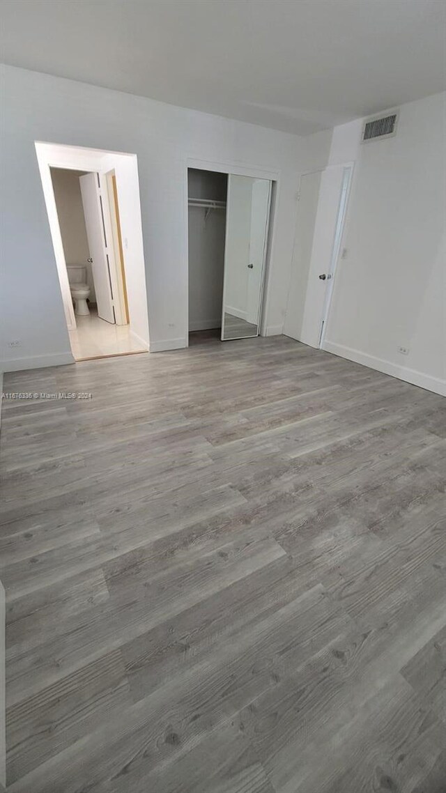 unfurnished bedroom featuring light hardwood / wood-style floors, ensuite bath, and a closet