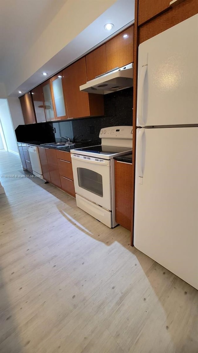 kitchen featuring light wood finished floors, brown cabinets, under cabinet range hood, tasteful backsplash, and white appliances