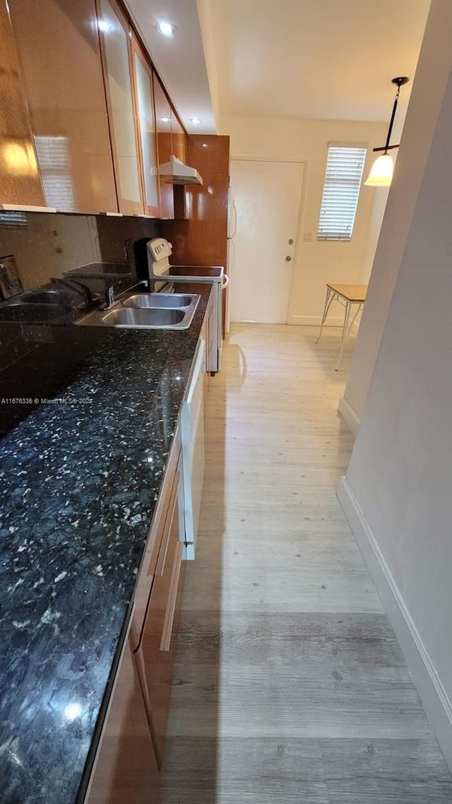 kitchen featuring stainless steel electric range oven, sink, dark stone counters, decorative light fixtures, and light wood-type flooring