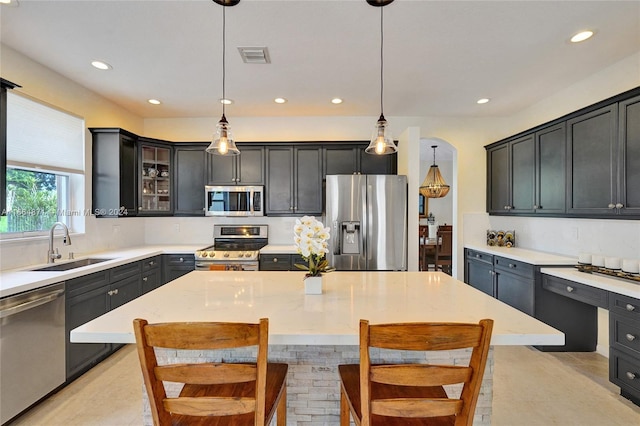 kitchen featuring a kitchen island, hanging light fixtures, stainless steel appliances, sink, and light stone countertops