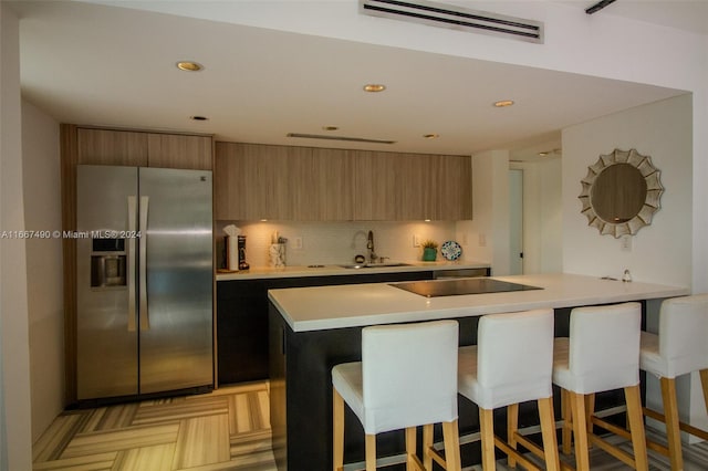 kitchen with black electric cooktop, a breakfast bar, sink, stainless steel refrigerator with ice dispenser, and backsplash