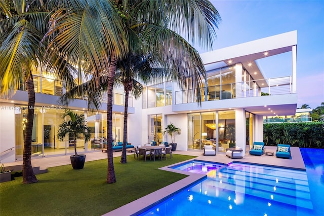 pool at dusk featuring an in ground hot tub, an outdoor living space, a patio, and a lawn