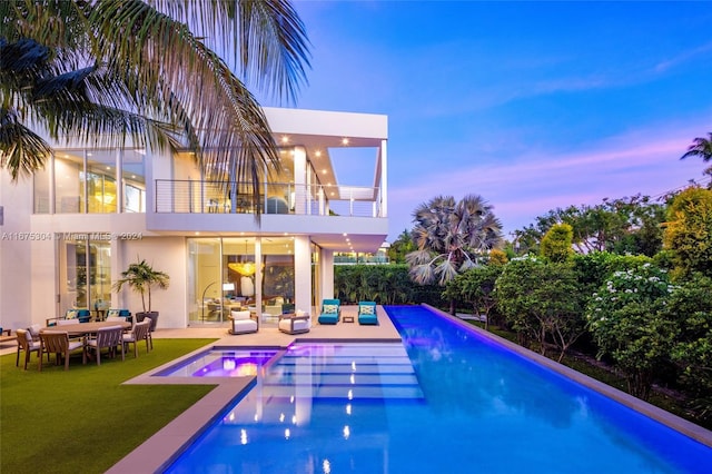 pool at dusk with a patio area and a lawn