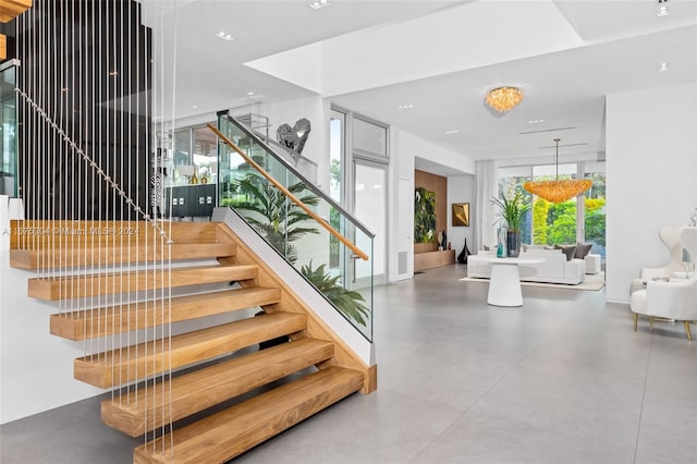 staircase with concrete floors and an inviting chandelier