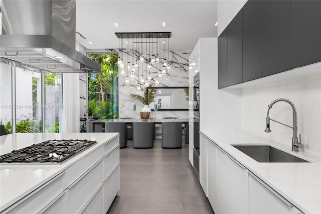 kitchen featuring white cabinets, stainless steel gas stovetop, pendant lighting, wall chimney exhaust hood, and sink