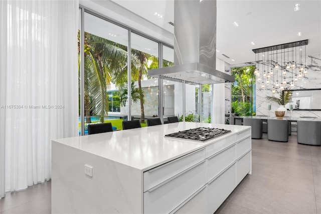 kitchen featuring island range hood, stainless steel gas cooktop, backsplash, a center island, and white cabinets