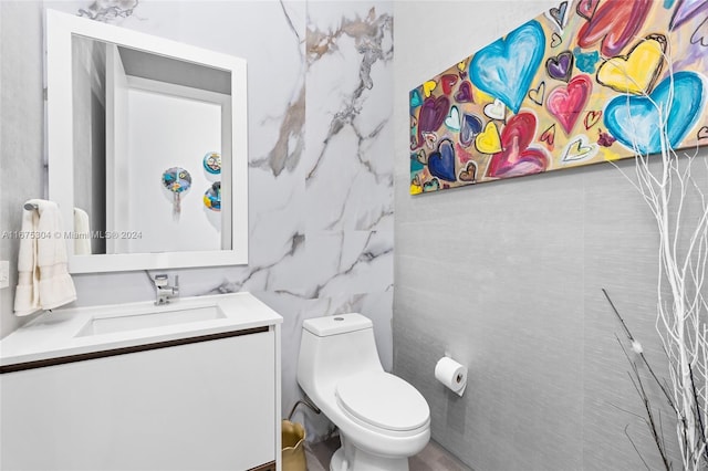 bathroom with toilet, vanity, and tile walls