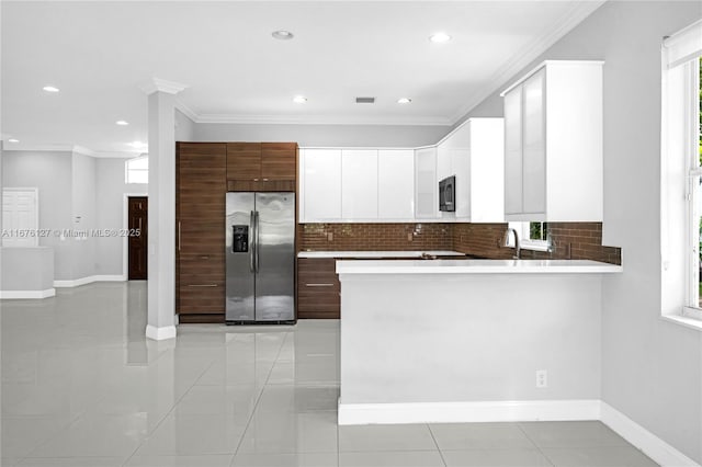 kitchen with crown molding, stainless steel fridge, white cabinetry, decorative backsplash, and kitchen peninsula