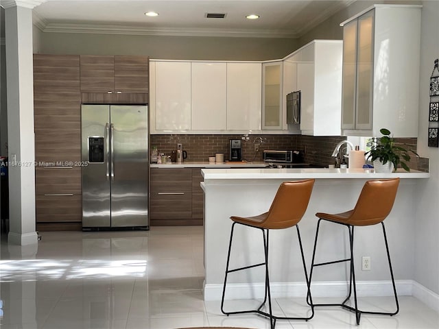 kitchen with crown molding, appliances with stainless steel finishes, white cabinetry, a kitchen breakfast bar, and tasteful backsplash