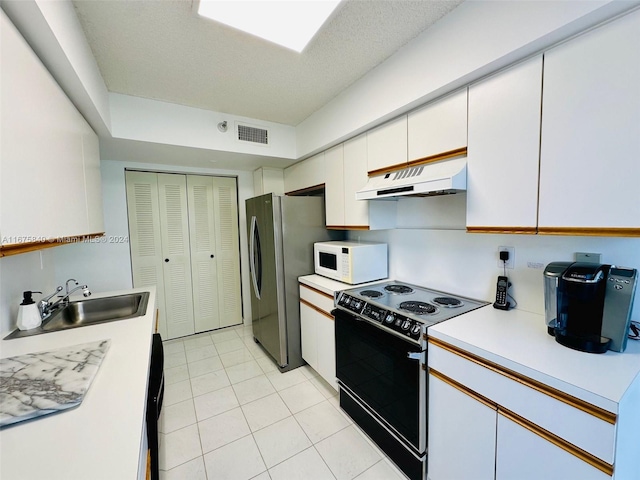 kitchen with light tile patterned flooring, stainless steel refrigerator, sink, black range with electric cooktop, and white cabinets