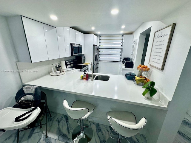 kitchen with sink, kitchen peninsula, white cabinetry, stainless steel appliances, and a kitchen bar