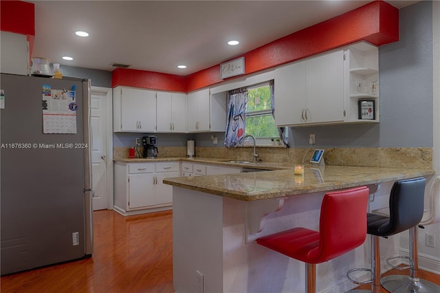 kitchen with stainless steel fridge, sink, kitchen peninsula, white cabinetry, and light hardwood / wood-style flooring