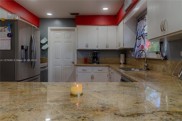 kitchen with light stone counters, white cabinets, stainless steel refrigerator with ice dispenser, and sink