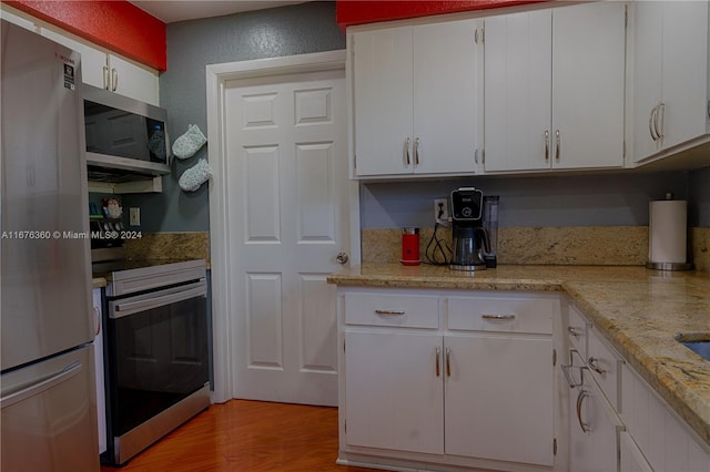 kitchen with light hardwood / wood-style floors, appliances with stainless steel finishes, light stone counters, and white cabinetry