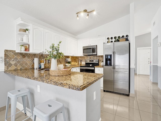 kitchen with backsplash, kitchen peninsula, dark stone countertops, lofted ceiling, and appliances with stainless steel finishes