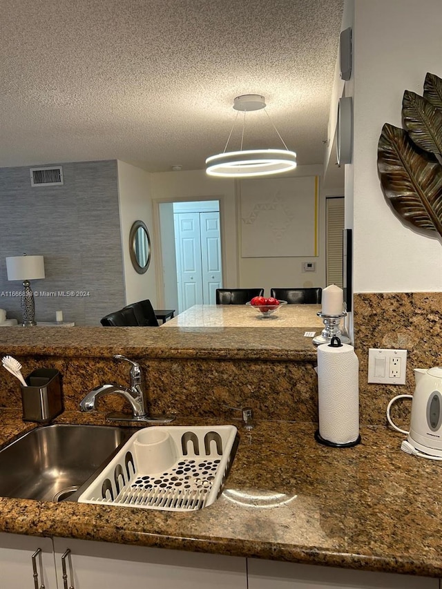 kitchen featuring dark stone countertops, a textured ceiling, hanging light fixtures, and sink