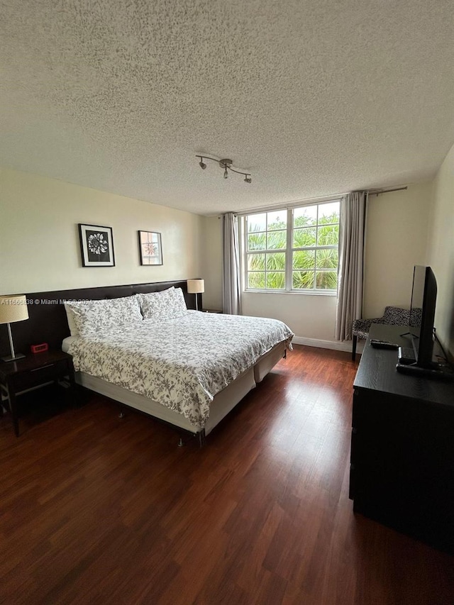 bedroom with track lighting, dark wood-type flooring, and a textured ceiling