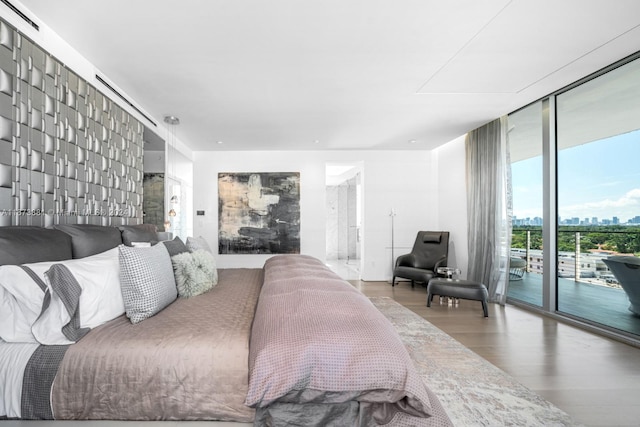 bedroom with wood-type flooring, access to outside, and a wall of windows