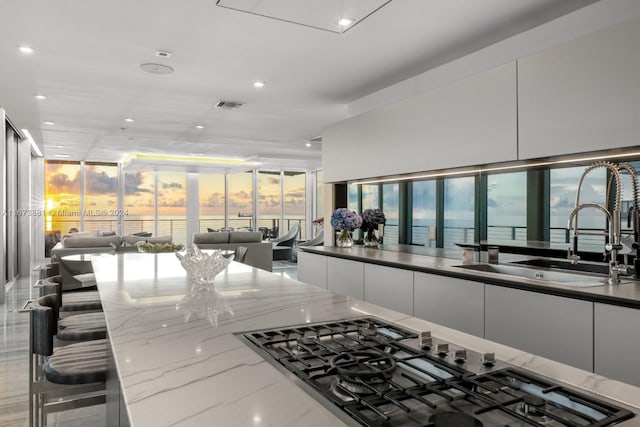 kitchen featuring dark stone counters, a breakfast bar, sink, white cabinets, and a large island