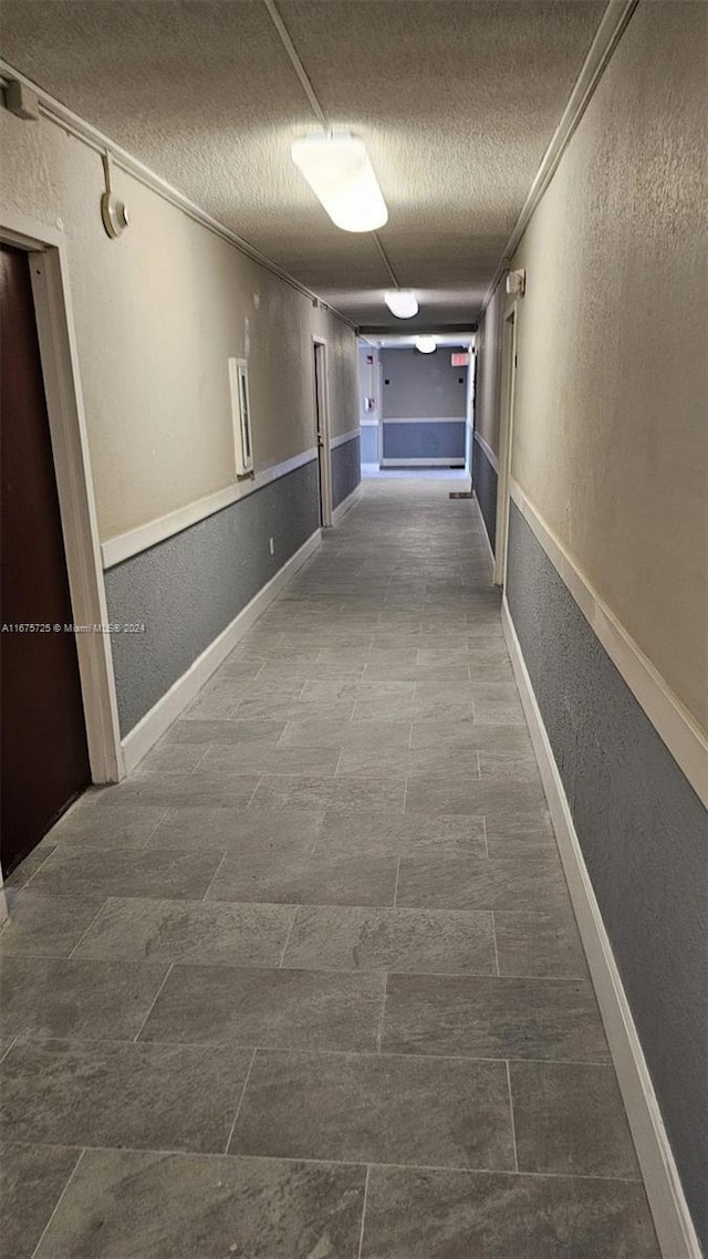 hall featuring a textured ceiling, a textured wall, and baseboards
