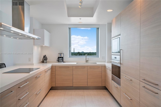 kitchen featuring wall chimney range hood, stainless steel oven, light brown cabinets, sink, and black electric stovetop