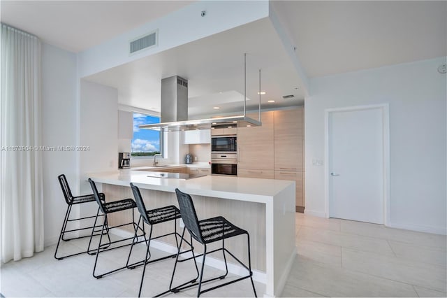 kitchen with light tile patterned floors, sink, kitchen peninsula, island range hood, and a breakfast bar area