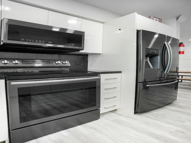 kitchen with white cabinets, appliances with stainless steel finishes, decorative backsplash, and light hardwood / wood-style flooring