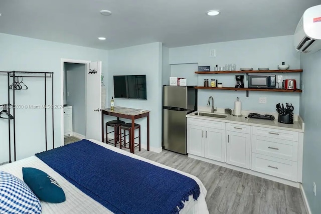 bedroom featuring a wall mounted air conditioner, stainless steel refrigerator, light hardwood / wood-style flooring, and sink