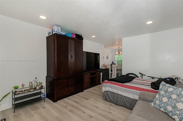 bedroom with a chandelier, light hardwood / wood-style flooring, and a textured ceiling