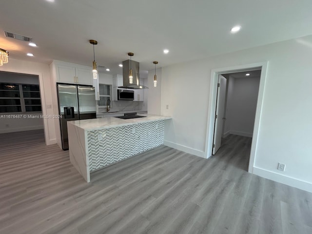 kitchen featuring wall chimney range hood, kitchen peninsula, light wood-type flooring, appliances with stainless steel finishes, and white cabinetry