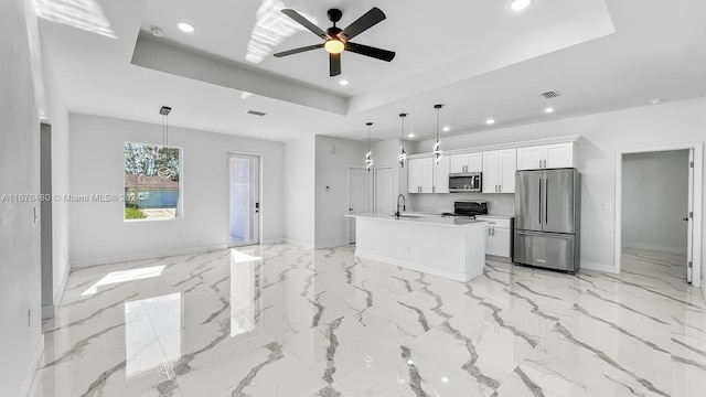 kitchen with appliances with stainless steel finishes, a raised ceiling, a kitchen island with sink, pendant lighting, and white cabinets