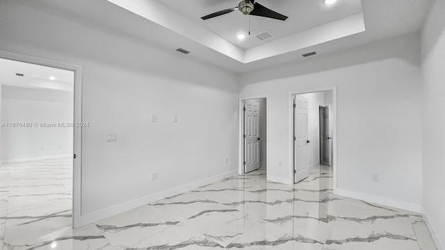 unfurnished bedroom with a tray ceiling, ensuite bath, and ceiling fan