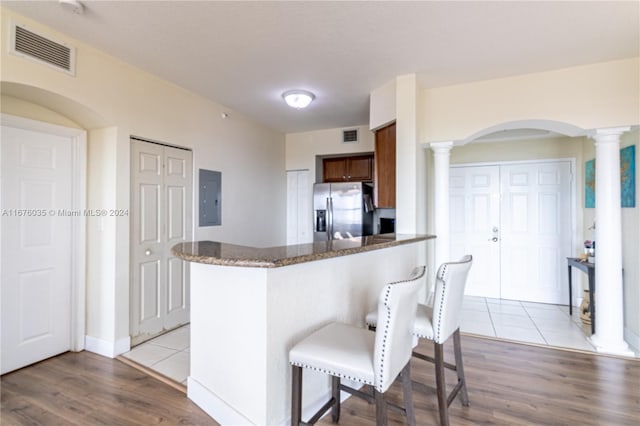 kitchen featuring light wood-type flooring, ornate columns, electric panel, a breakfast bar area, and stainless steel refrigerator with ice dispenser