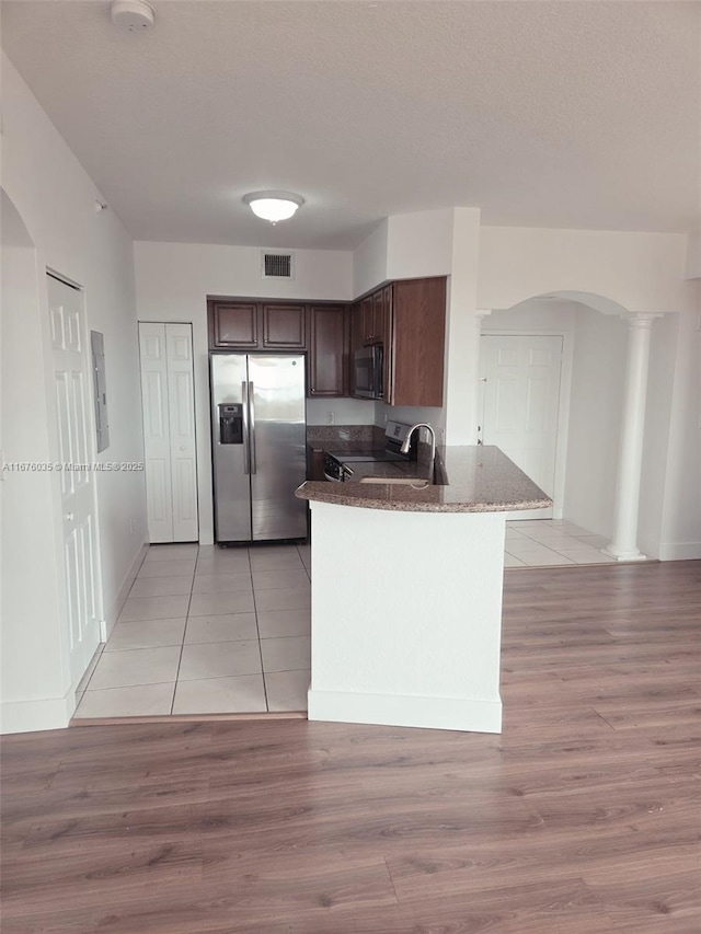 kitchen with stainless steel appliances, arched walkways, dark brown cabinetry, and visible vents