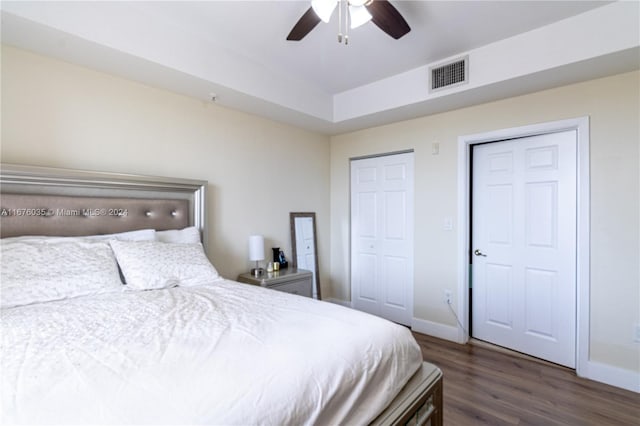 bedroom with ceiling fan, multiple closets, and dark hardwood / wood-style flooring