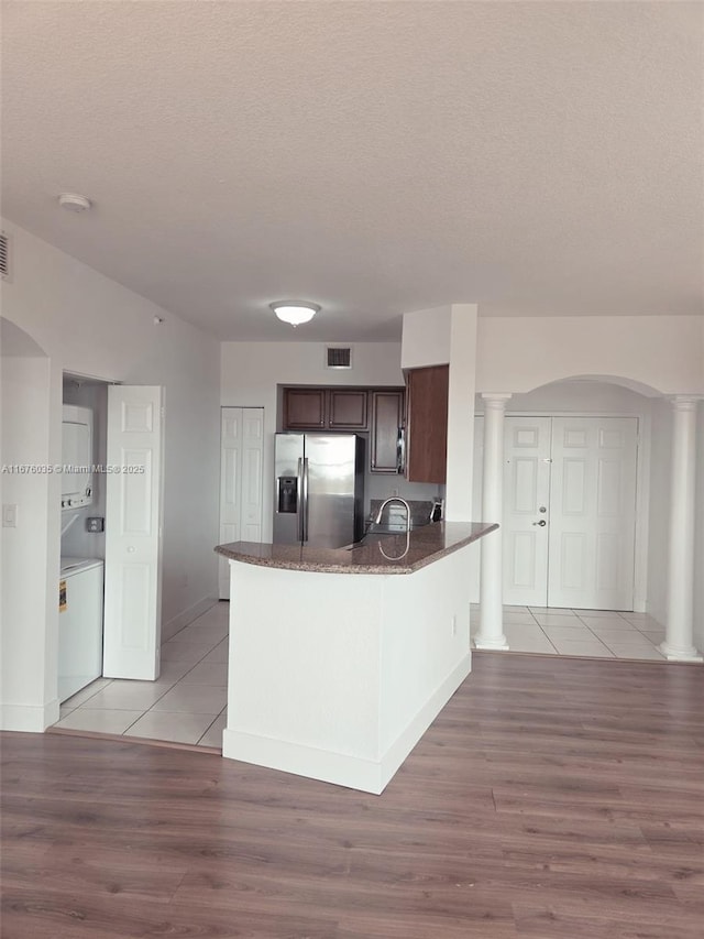 kitchen with visible vents, decorative columns, dark brown cabinets, stacked washer / drying machine, and stainless steel fridge